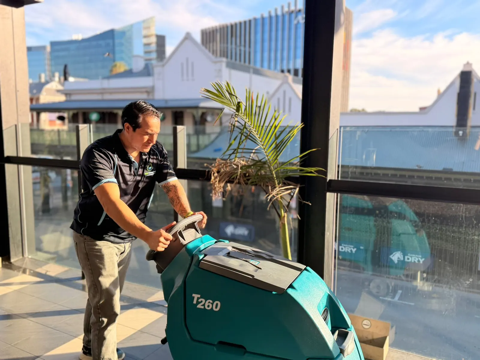 SJV Cleaning technician operating a floor scrubber on a glass-walled balcony