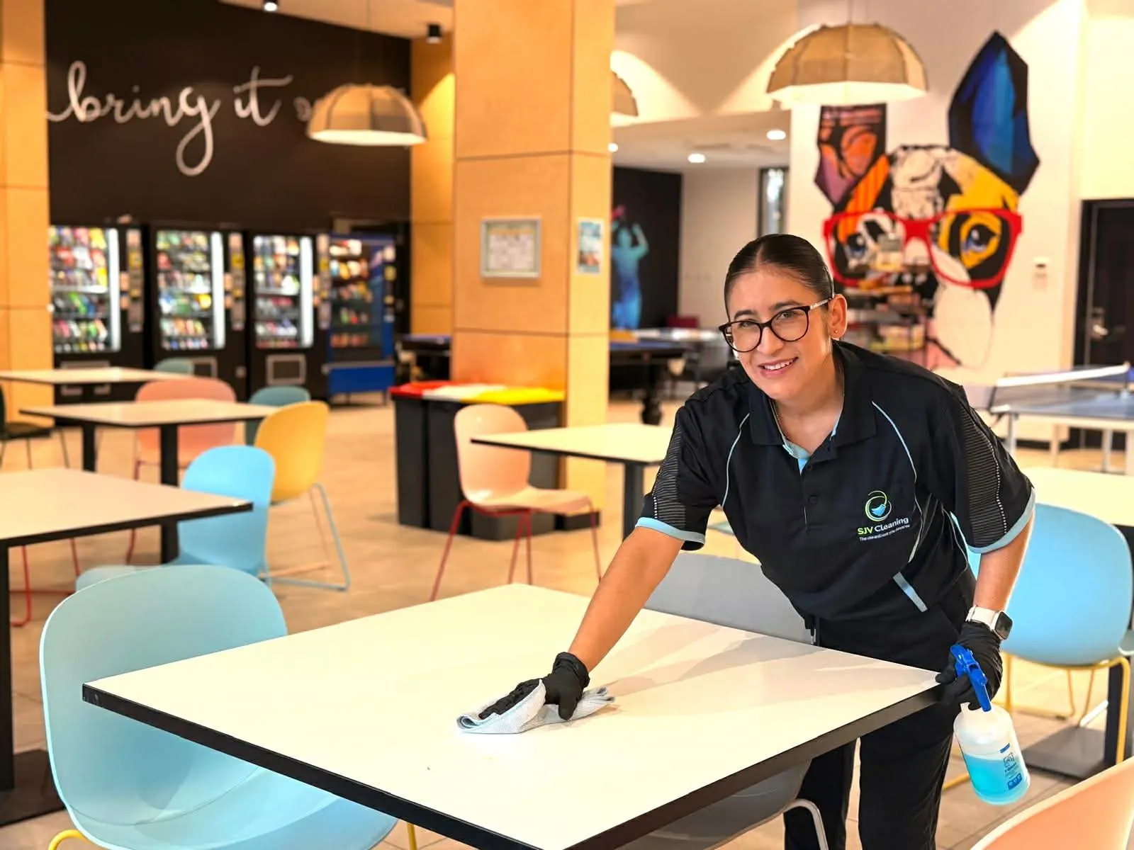 SJV Cleaning team member in gloves sanitising a table in a food court dining area